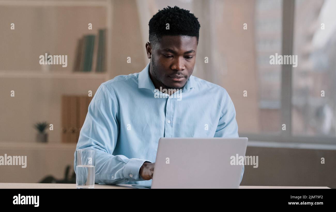Afrikanischer Mann beschäftigt Arbeiter amerikanischer Geschäftsmann Kerl Student sitzen zu Hause Büro Eingabe auf Computer fertig Online-Arbeit machen tägliche Aufgaben durstig fühlen Stockfoto