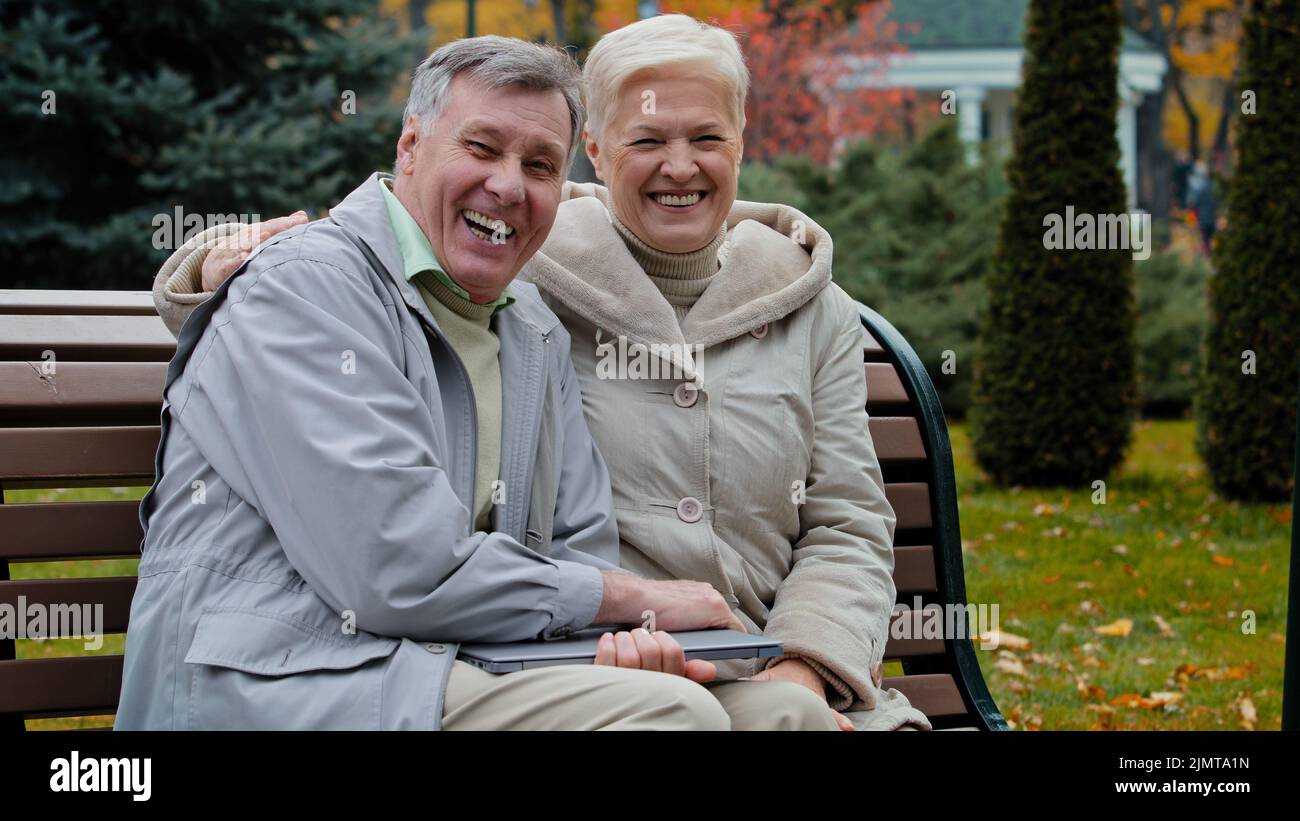Kaukasisch verheiratetes Paar Familie im Ruhestand 60s Personen Mann Frau winkende Hände hallo Auf Wiedersehen Geste Ältere Großeltern sitzen auf der Bank im Herbstpark Stockfoto