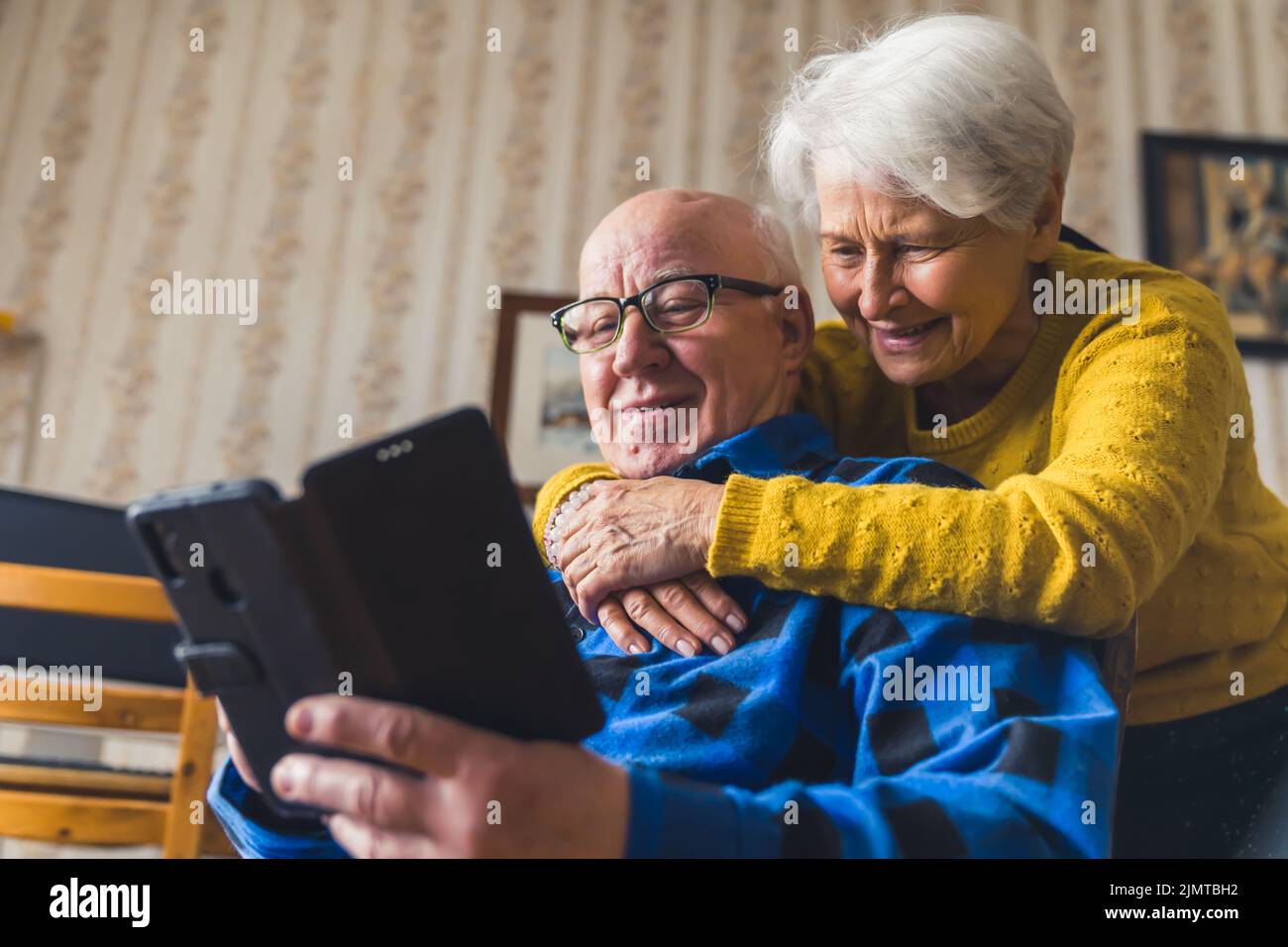 Glückliches kaukasisches Seniorenpaar, das lächelt und umarmt, während es mit ihren Kindern im facetime-Videochat über ein neues Smartphone spricht. Hochwertige Fotos Stockfoto
