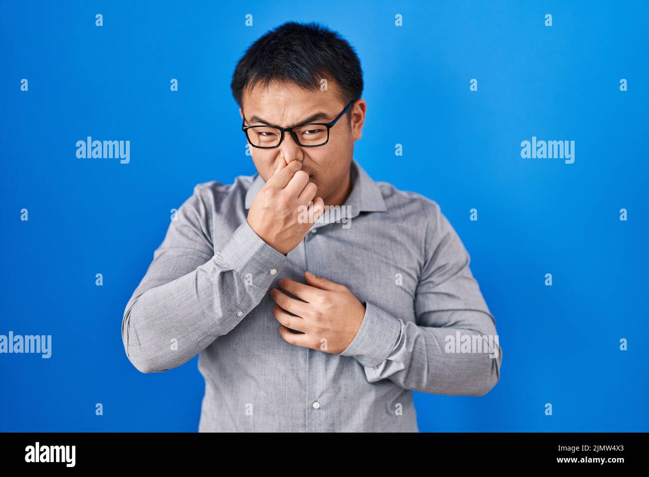 Junger chinese, der auf blauem Hintergrund steht, riecht etwas stinkendes und ekelhaftes