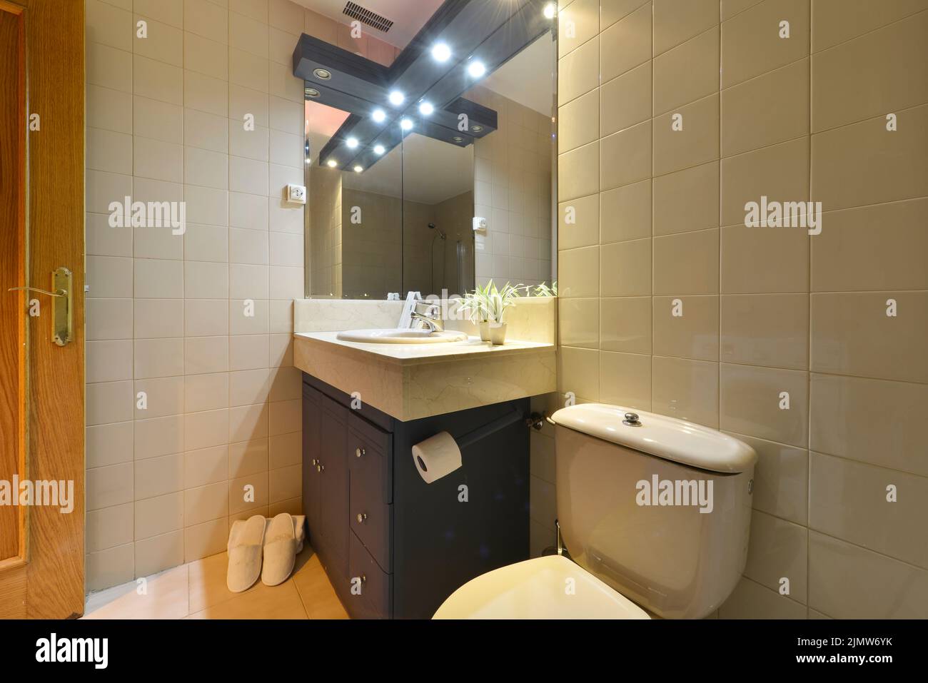 Badezimmer mit dunklen Holzschränken, rahmenlosen Spiegeln an beiden Seiten und weißen Hausschuhen Stockfoto