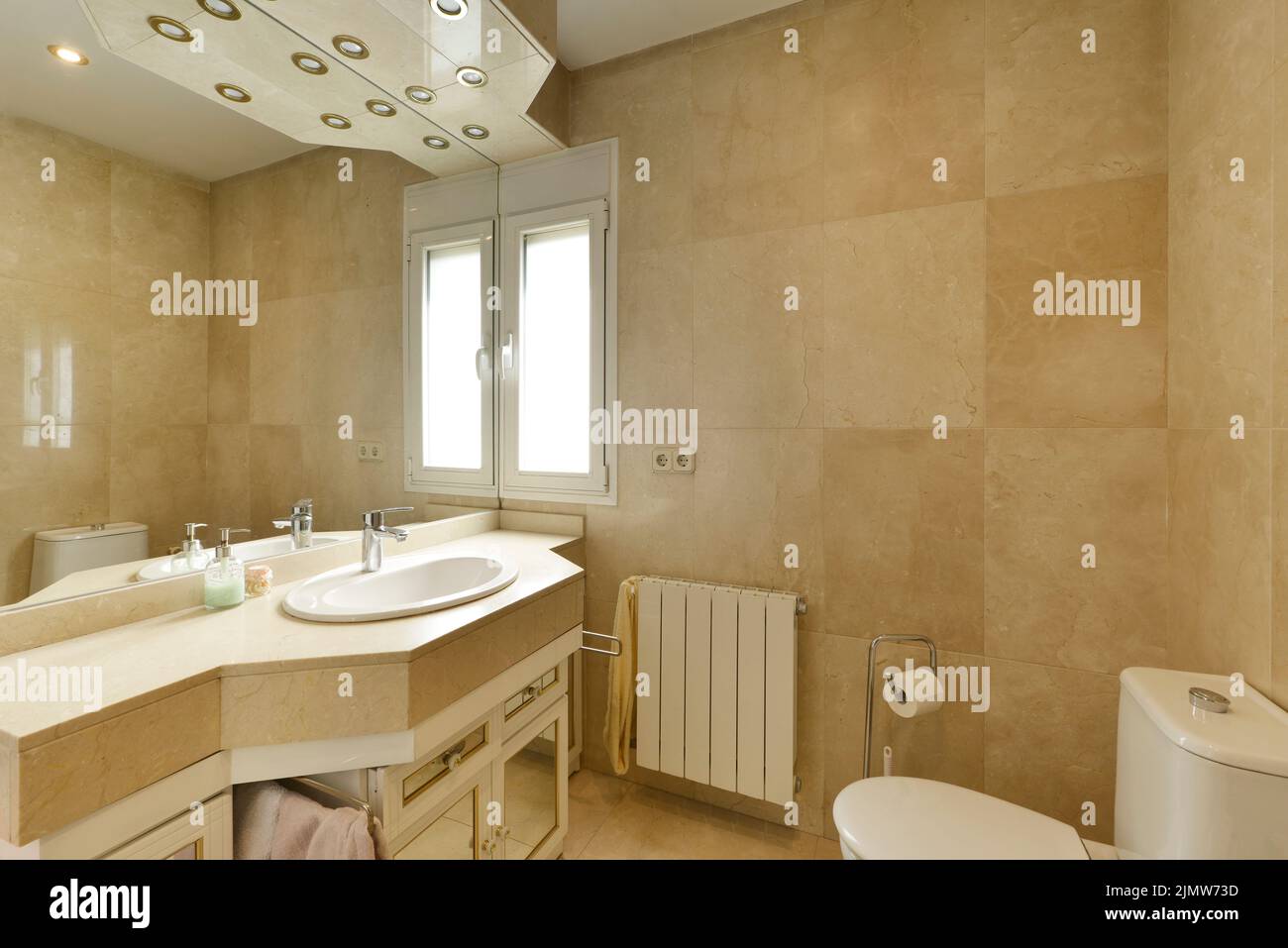 Badezimmer mit cremefarbenem Marmorwaschbecken, großem rahmenlosen Wandspiegel und unbeleuchteten Halogenlampen Stockfoto