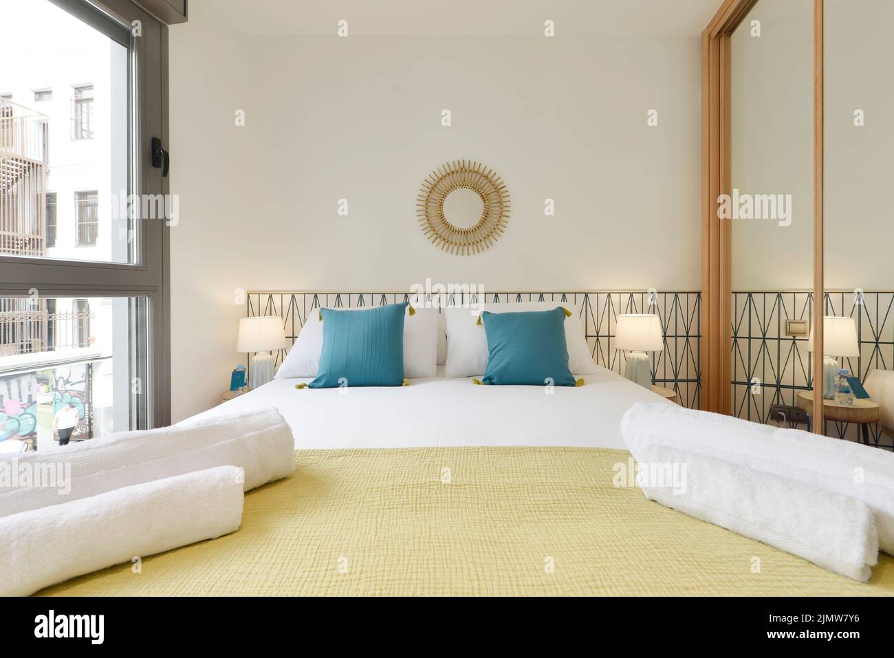 Schlafzimmer mit moderner Dekoration, Einbauschrank mit Spiegelschiebetüren und Holzkanten, blauen Kissen auf den Kissen und einem Fenster Stockfoto