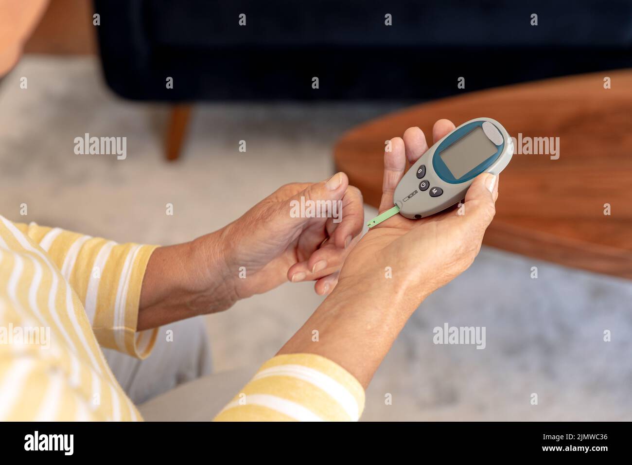 Mittlere Abteilung einer älteren kaukasischen Frau, die ihren Blutzucker mit Glucometer zu Hause misst Stockfoto