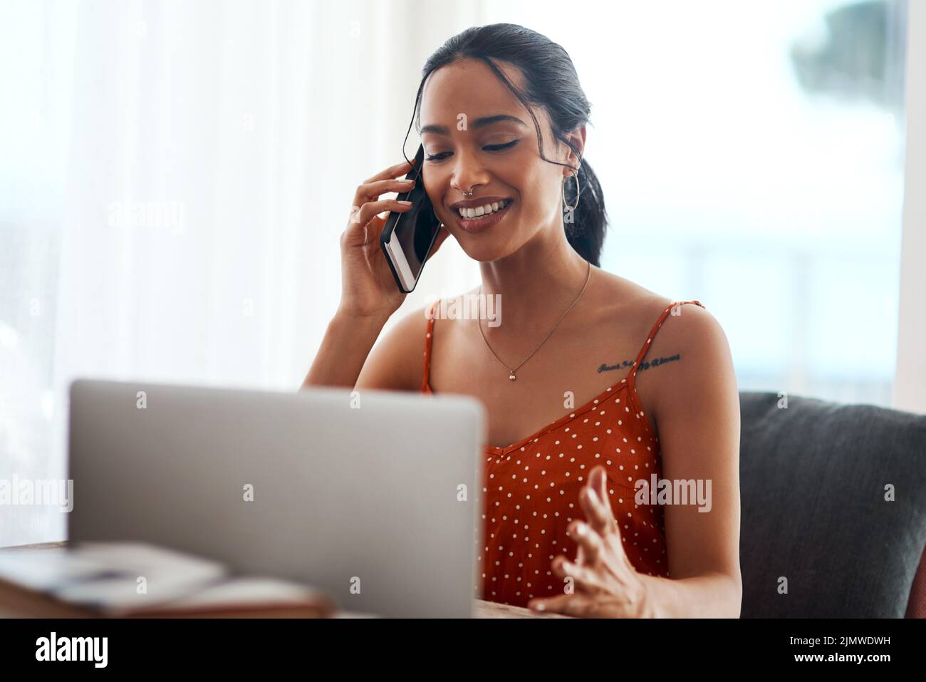 Die Arbeit von zu Hause aus ist so praktisch: Eine attraktive junge Geschäftsfrau sitzt in ihrem Büro und nutzt ihren Laptop während eines Telefonanrufs. Stockfoto