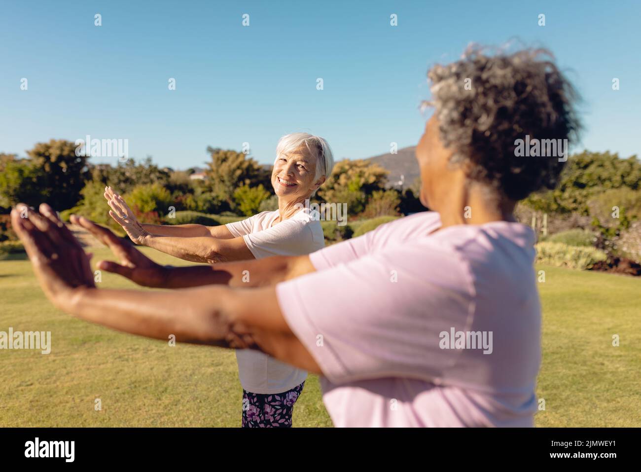 Lächelnde, multirassische Senioren, die sich im Hof des Altersheims die Hände gegen den klaren Himmel strecken Stockfoto