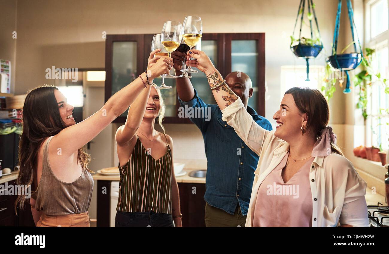 Heben Sie Ihre Gläser. Eine Gruppe von fröhlichen jungen Freunden mit einem feierlichen Toast mit Getränken, während in der Küche zu Hause Essen zubereiten stehen. Stockfoto