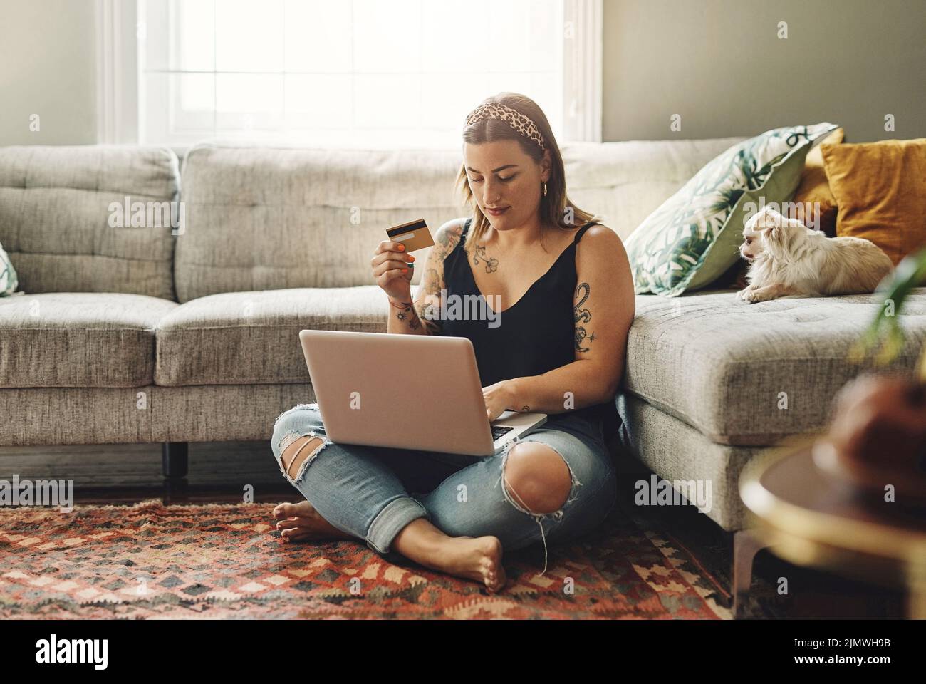 Ich denke, es ist an der Zeit, Hundefutter aufzutoben. Eine junge Frau, die zu Hause einen Laptop und eine Kreditkarte in ihrem Wohnzimmer benutzt. Stockfoto