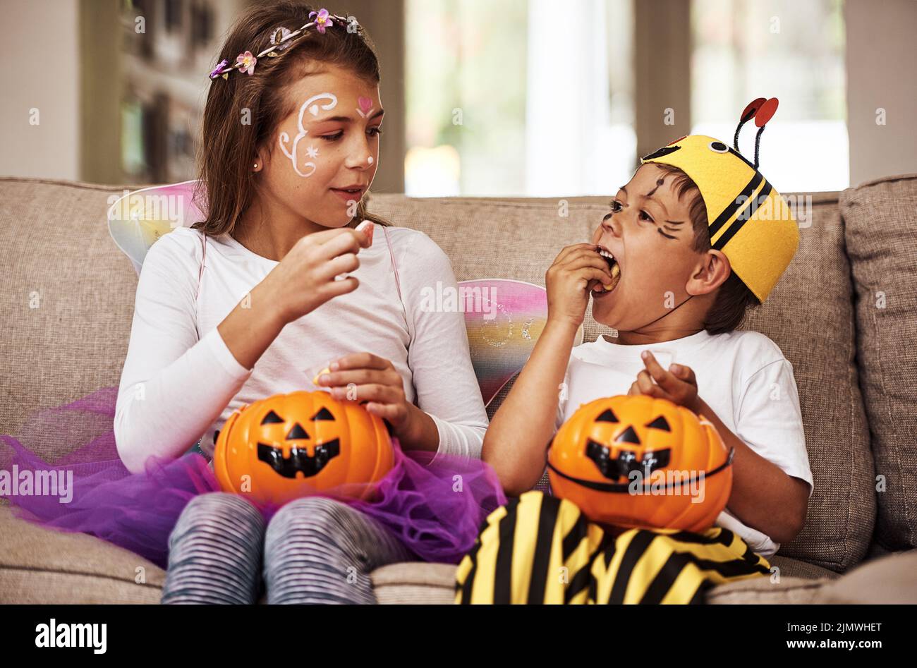 Ein junger Bruder und eine Schwester essen ihre Halloween-Süßigkeiten, während sie zu Hause auf ihrem Sofa sitzen. Stockfoto