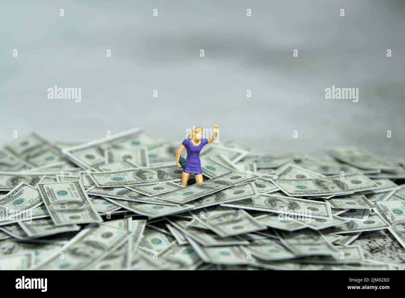 Miniatur Menschen Figur Spielzeug Fotografie. Konzept für Inflation und Rezession. Eine Frau ertrank in einem Haufen Dollargeld. Geschluckt von Schulden und ansteigendem Foo Stockfoto