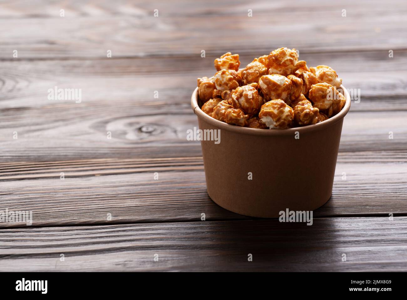 Karamellisiertes Popcorn im Papiereimer auf dem hölzernen Küchentisch Stockfoto