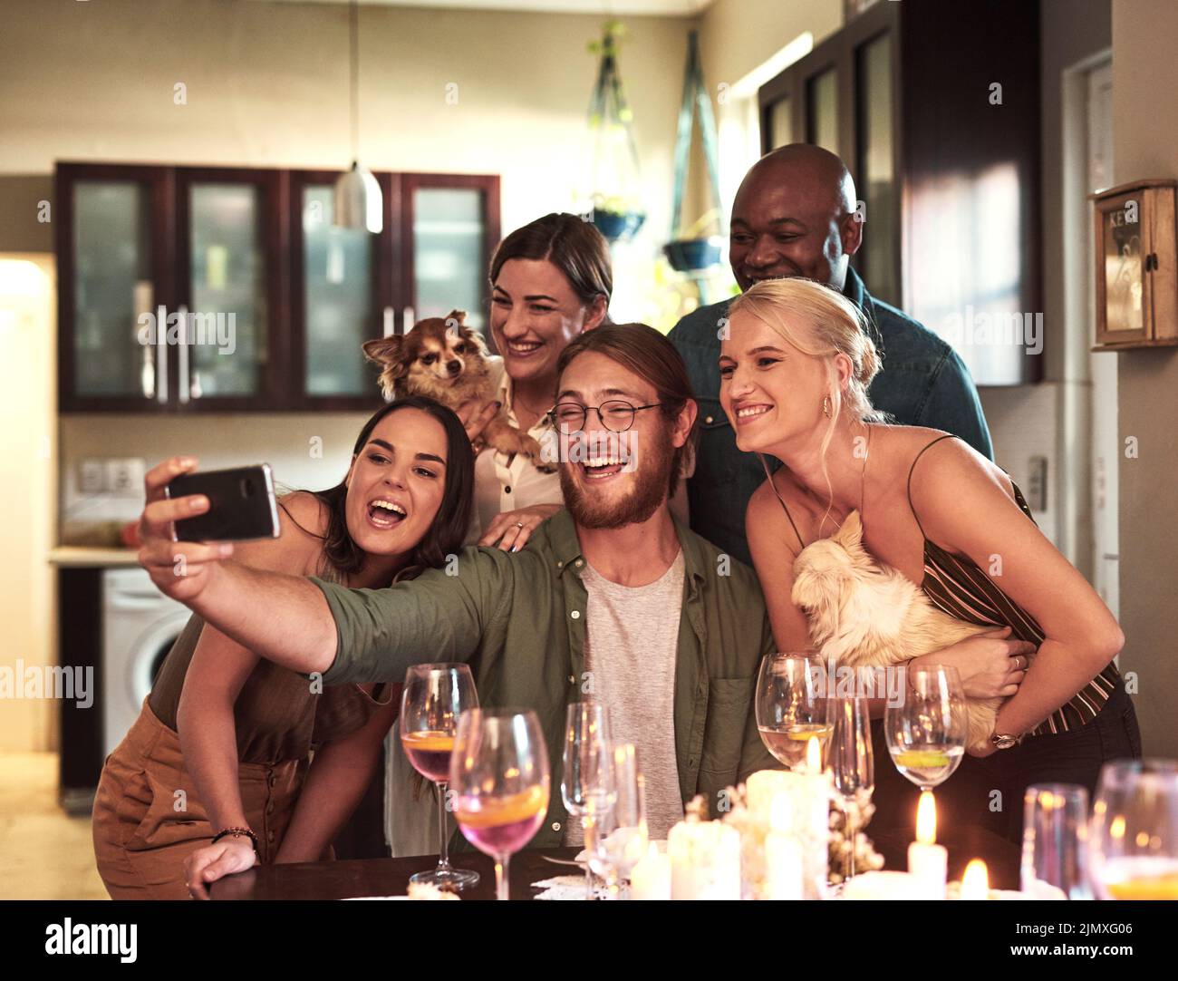 Zeit für ein schnelles Foto. Eine Gruppe fröhlicher junger Freunde, die zusammen mit einem Handy ein Selbstporträt während einer Dinner-Party zu Hause machen. Stockfoto