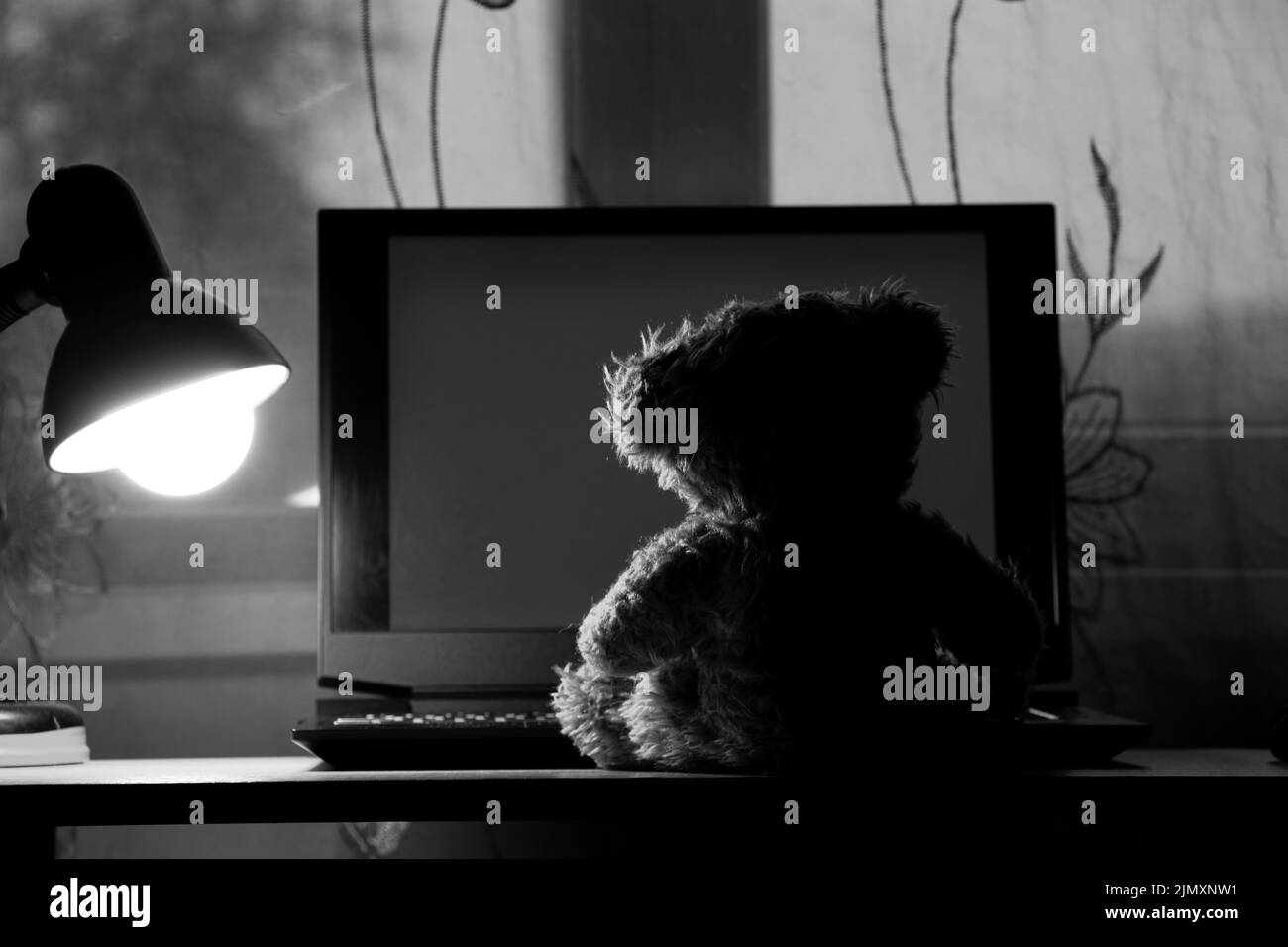 teddybär für Kinder sitzt mit einem Laptop auf dem Tisch, trägt nachts eine Tischlampe in den Schlafzimmern, trägt Fenster, Einsamkeit, Freude in a la Stockfoto