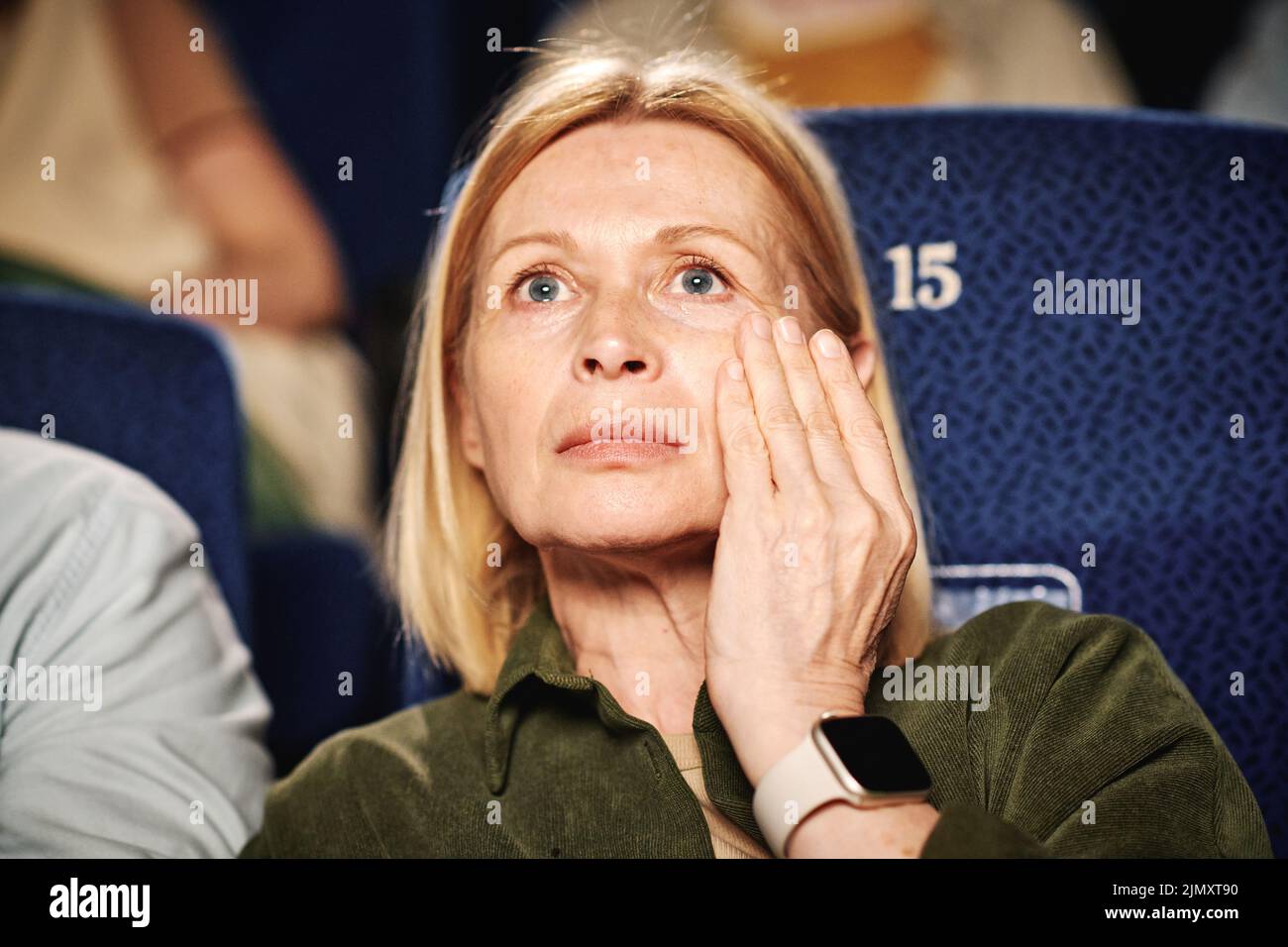Portrait der erwachsenen kaukasischen Frau, die einen tragischen Film im Kino sieht und Tränen mit der Hand abwischt Stockfoto
