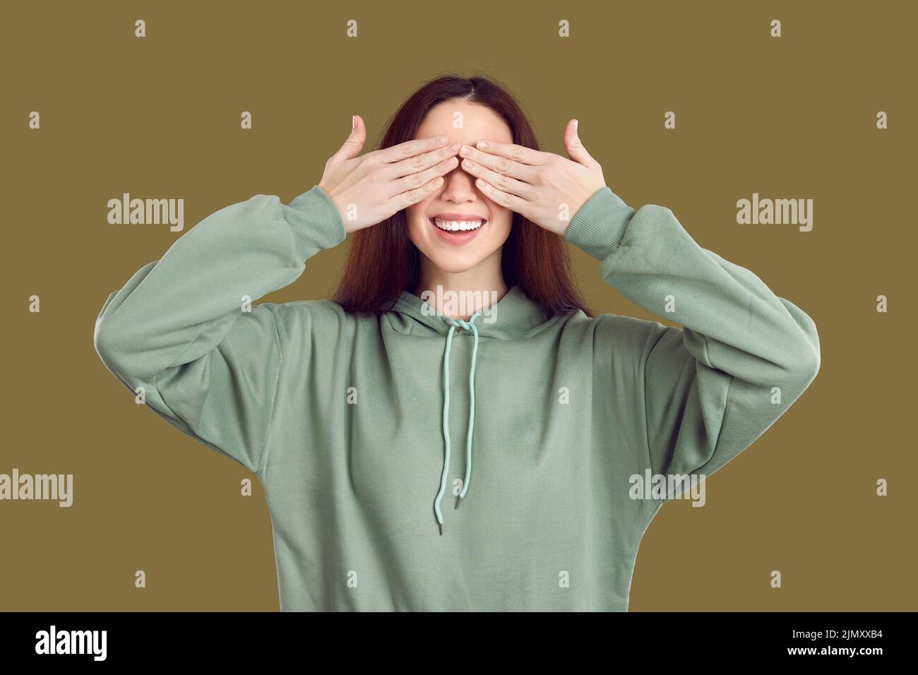 Lustige lächelnde Frau in Erwartung von etwas Interessantes schließt ihre Augen mit ihren Händen. Stockfoto