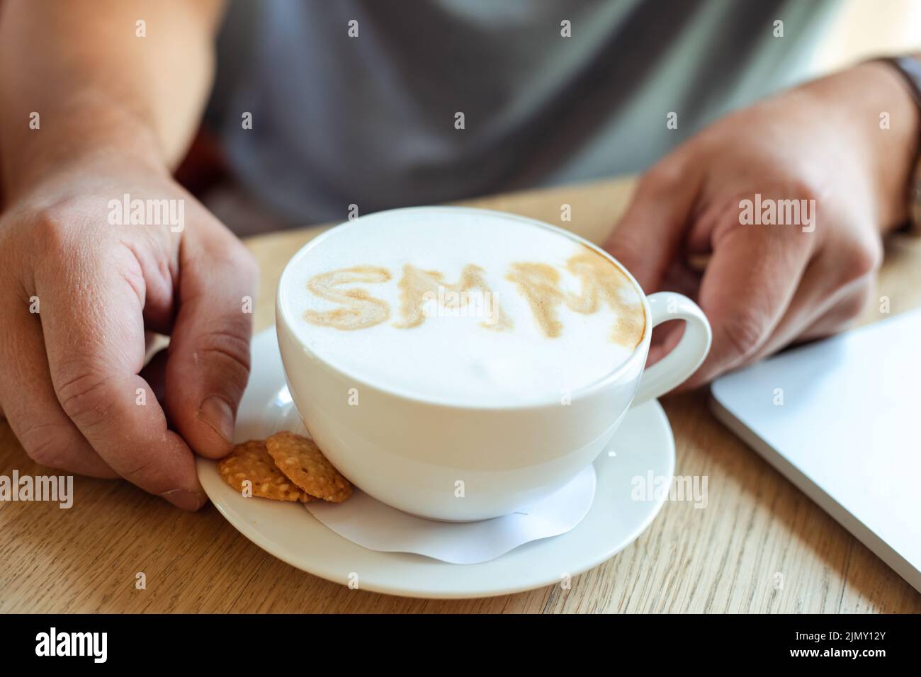 Hände eines Geschäftsmanns, der eine Tasse Kaffee mit heißem Geschmack und weißem Schaum aus der Nähe auf dem Tisch hält. Social Media Marketing, SMM, Promotion, leckere Getränke in Stockfoto