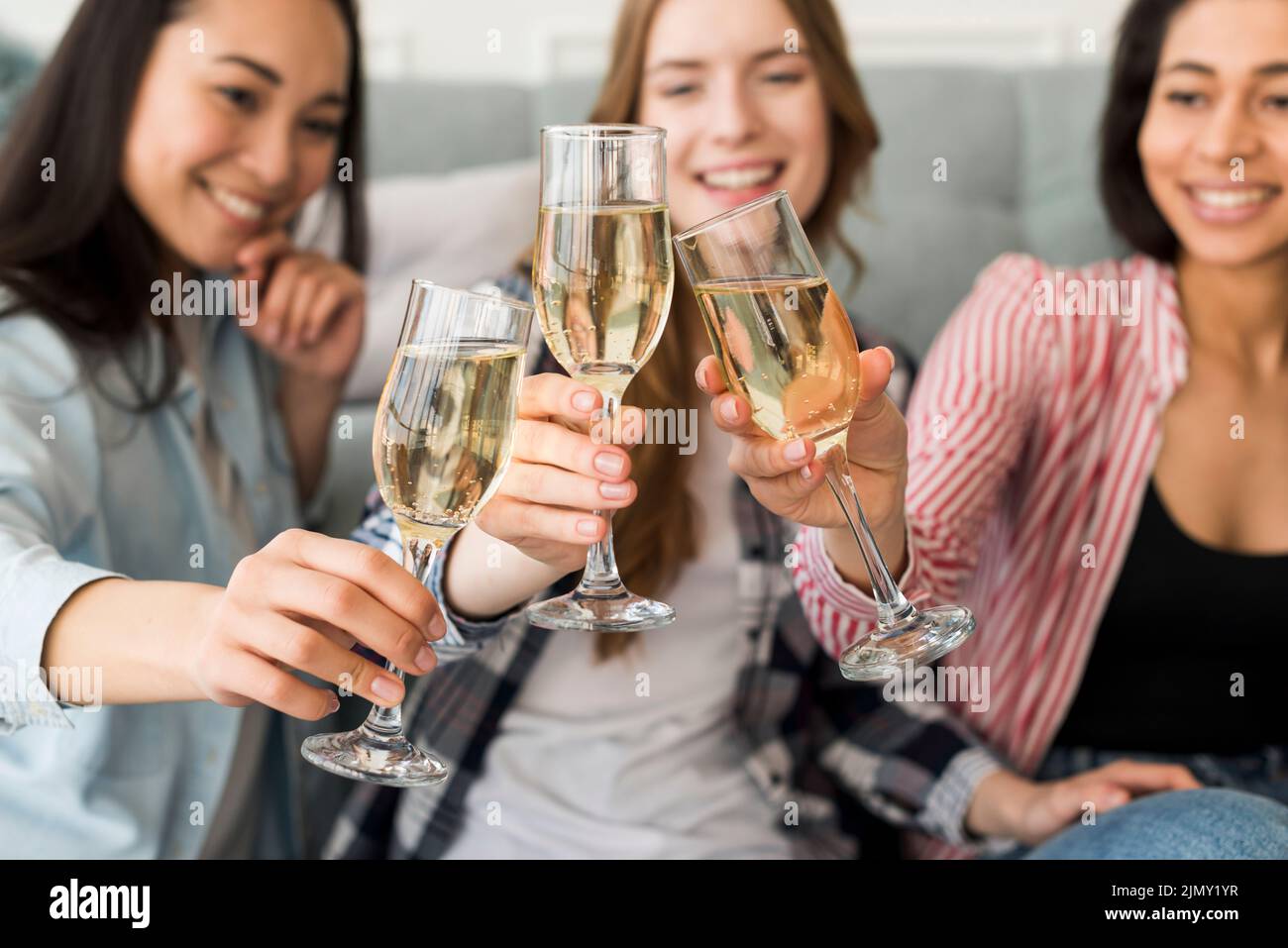 Lächelnde sitzende Mädchen halten Gläser zusammen klirren Stockfoto
