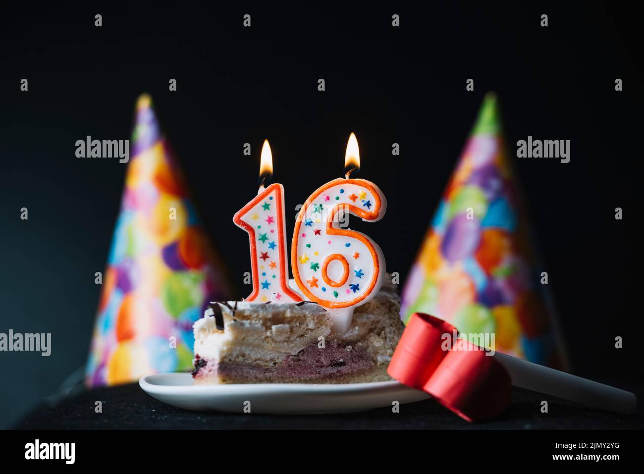 Zahl 16 Geburtstag brennende Kerze Scheibe Kuchen mit Party Hut Party Horn Gebläse Stockfoto