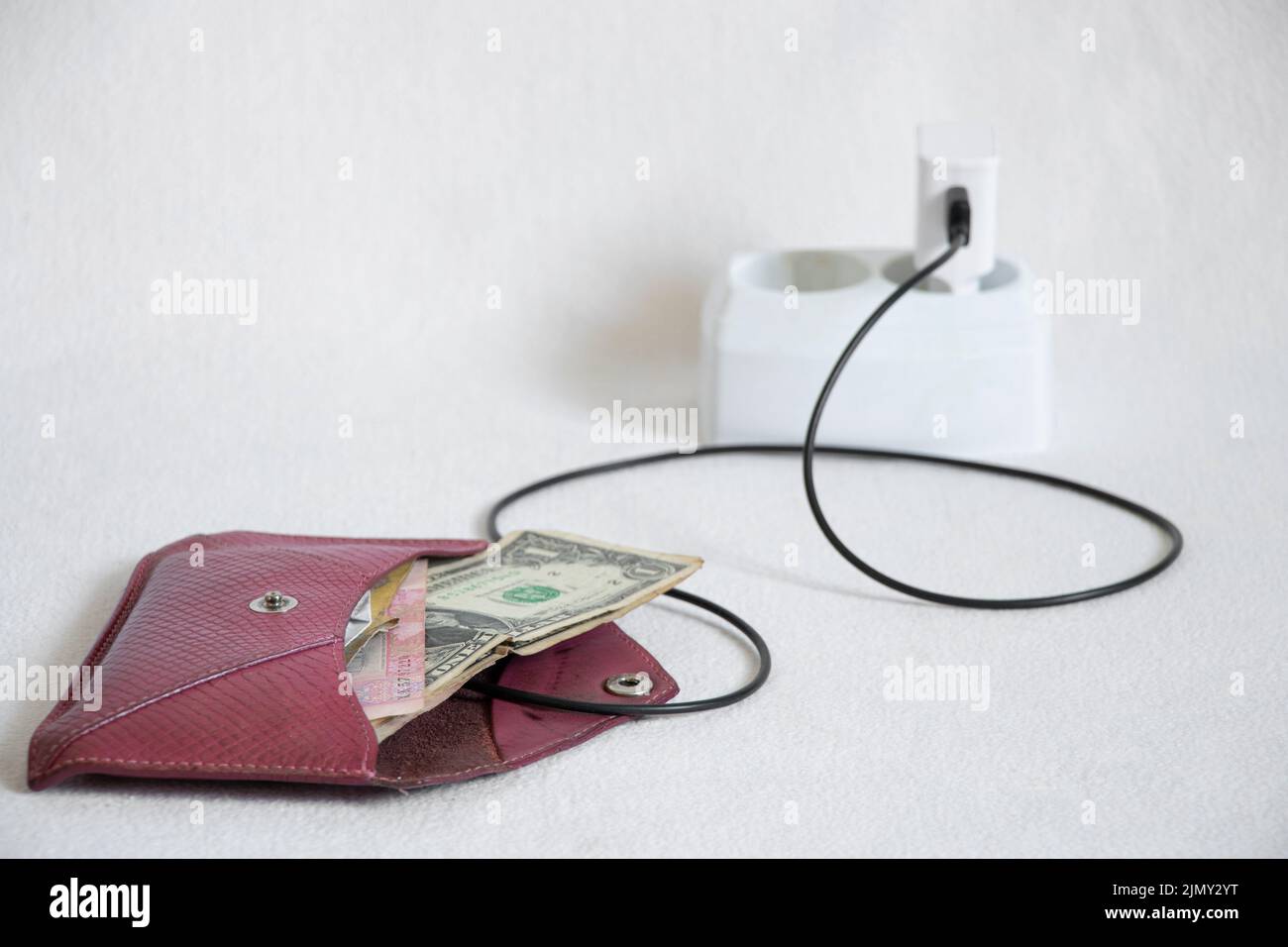 Eine Brieftasche mit Geld steht auf Aufladen in einer Steckdose auf weißem Hintergrund, Finanzen und Erfolg Stockfoto