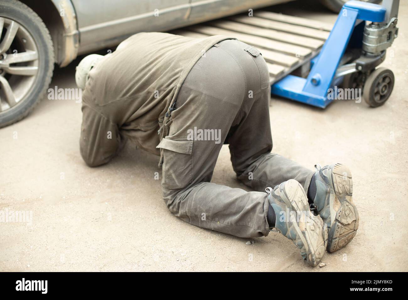 Der Mann schaut unter das Auto. Radwechsel. Reparatur des Transports. Es ist eine schwierige Aufgabe. Mann auf dem Bürgersteig. Stockfoto
