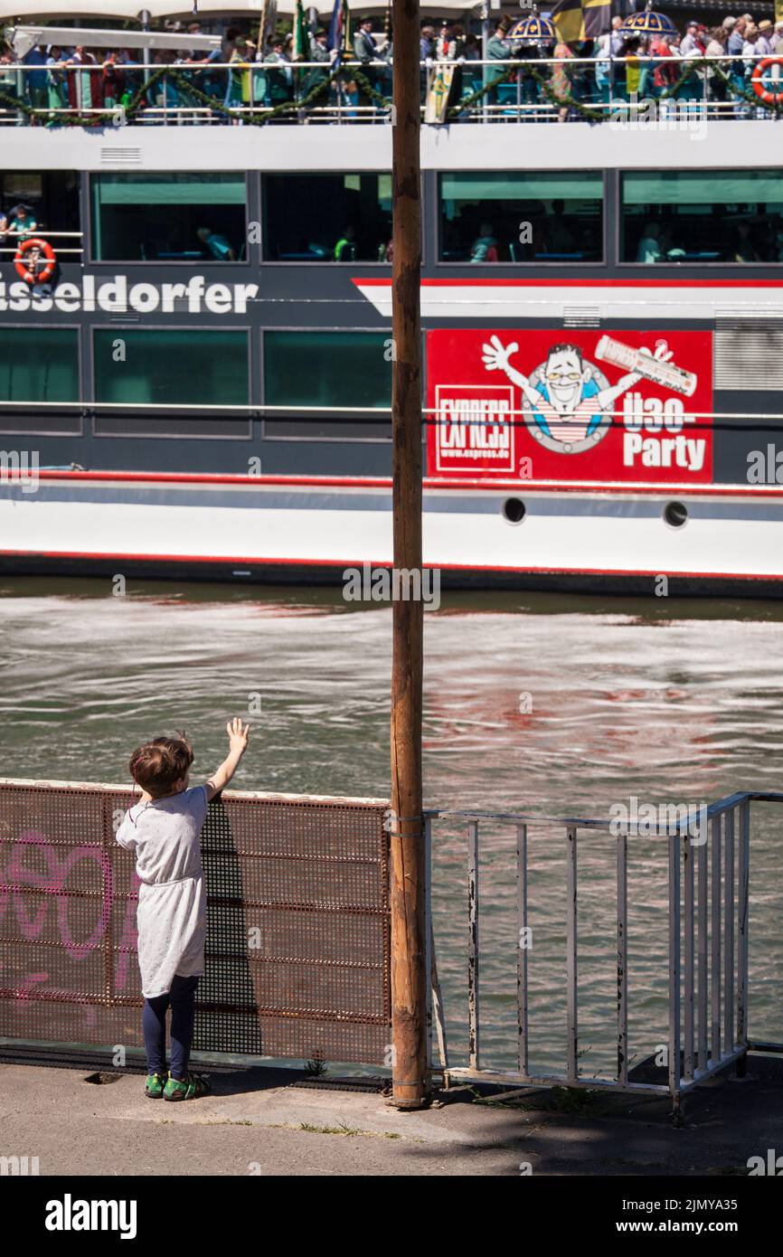 Ein Kind steht am Rheinufer im Landkreis Mülheim und winkt zu einem vorbeifahrenden Schiff, Köln. Ein Kind steht am Rheinufer im Stad Stockfoto