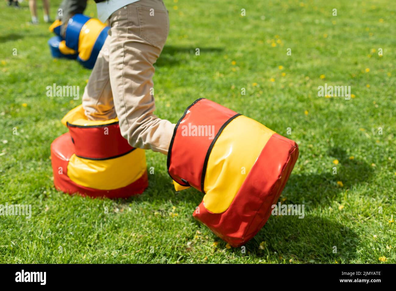 Lustige Schuhe für das Spiel. Spaß Urlaub des Kindes im Sommer. Unterhaltung auf grünem Gras. Spielen auf dem Rasen. Kind in unbequemen Schuhen. Stockfoto