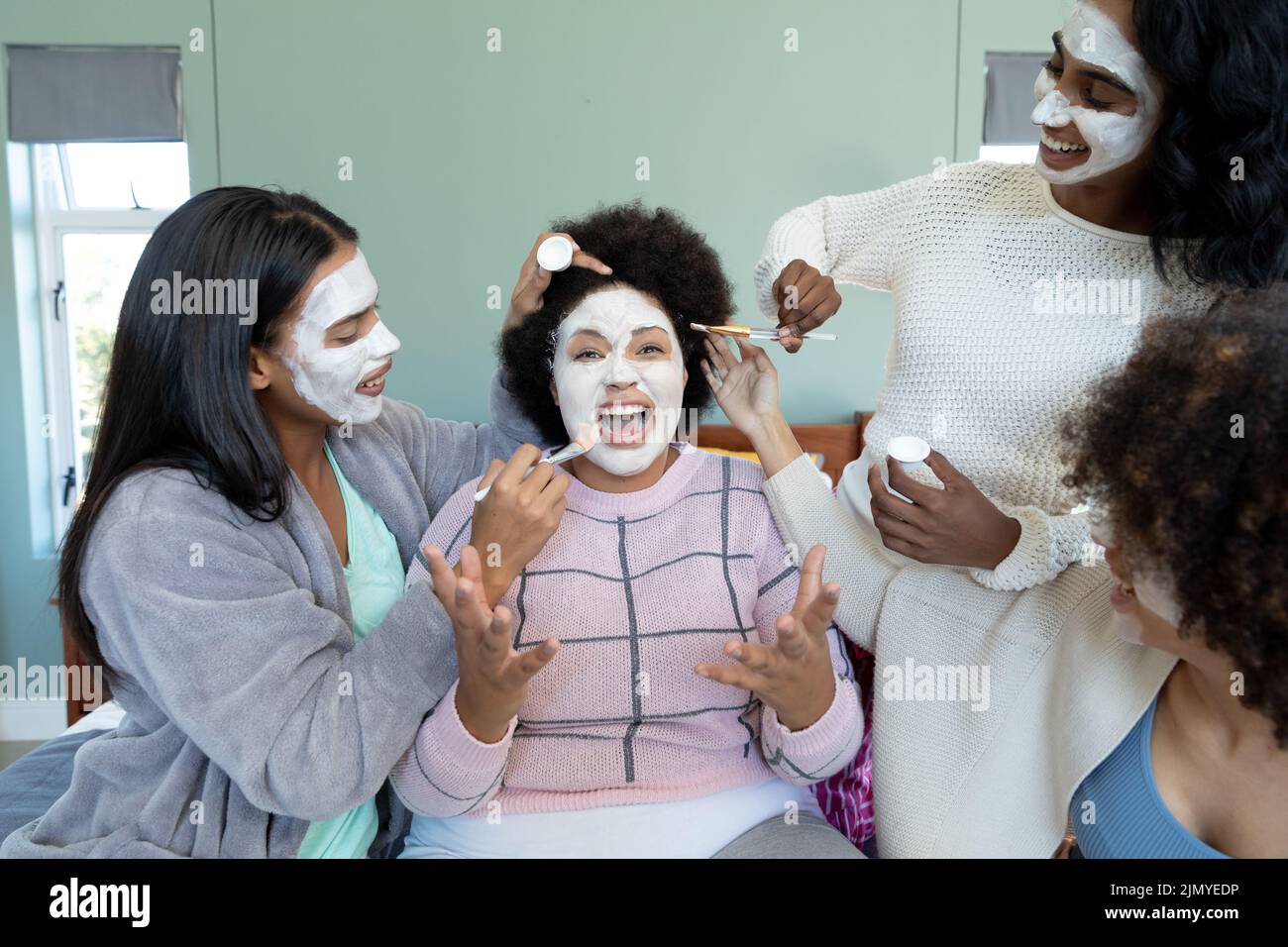 Biracial junge Frauen Anwendung Schönheitscreme auf fröhliche Freund Gesicht mit afro Haar Schreien Stockfoto