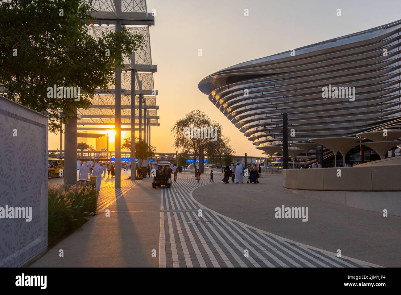 VAE, Dubai - 30. November 2021: Ausstellung EXPO 2020. Menschen gehen zwischen Pavillons entlang. Ausstellungshalle Mobilität in den Abendstrahlen des Sonnenuntergangs. Stockfoto