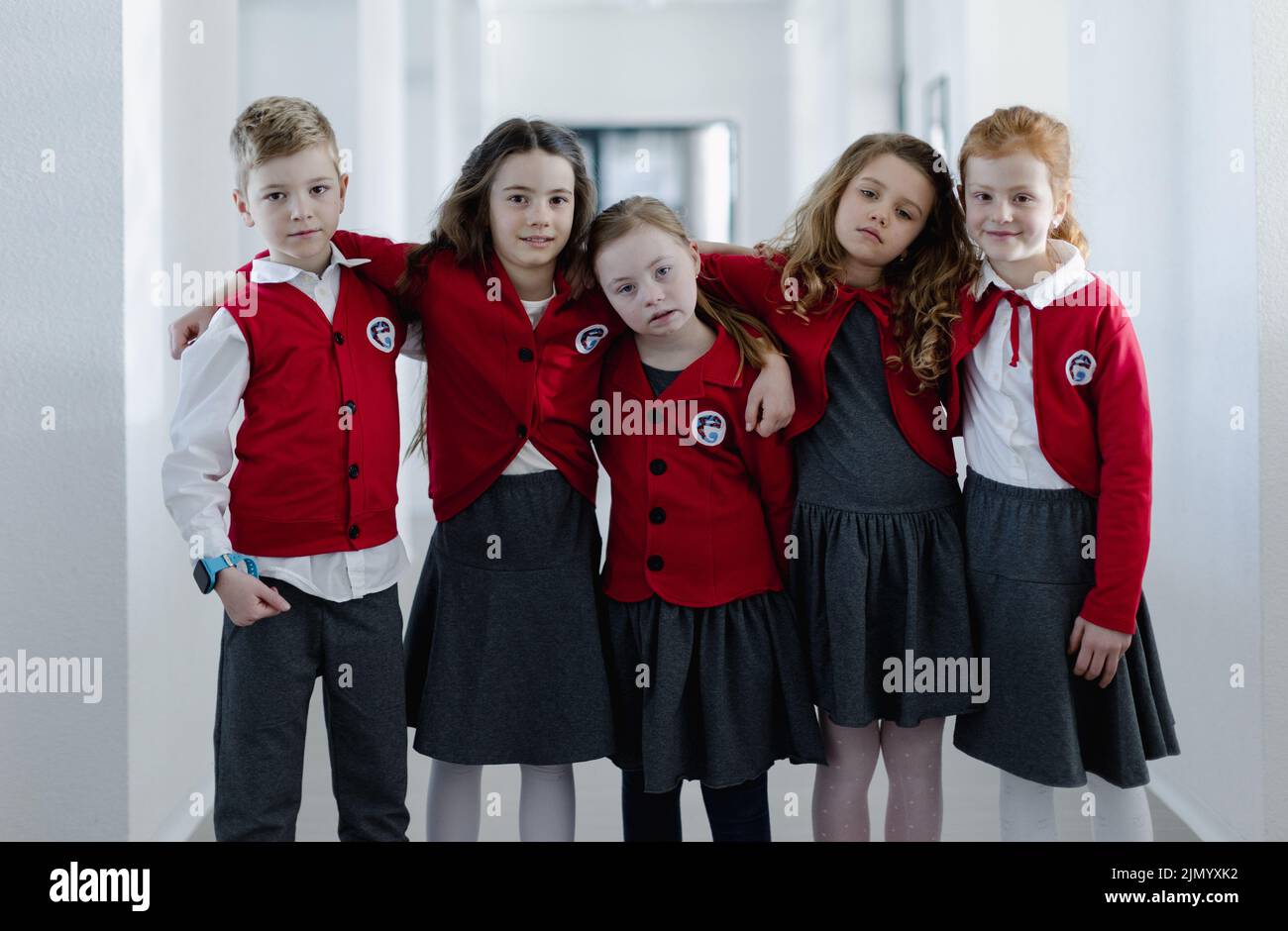 Fröhliches Schulkind mit Down-Syndrom, das mit ihren Klassenkameraden im Schulkorridor steht und die Kamera anschaut. Stockfoto