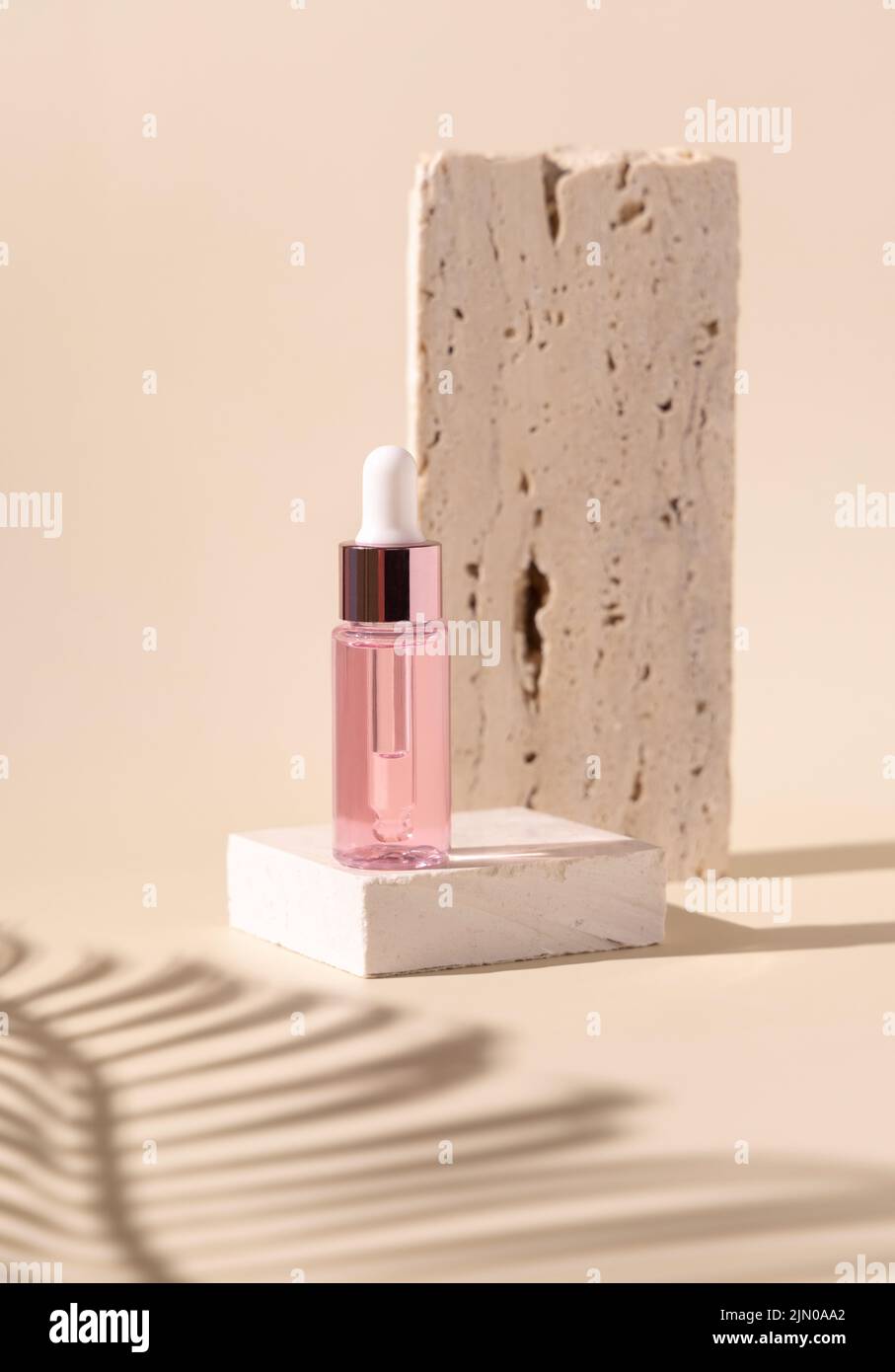 Tropfflasche auf Travertin-Stein in der Nähe von weißen Orchideenblüten und Palmenblatt-Schatten auf hellgelb, Nahaufnahme, Mockup. Hautpflege Beauty-Produkt, essentia Stockfoto