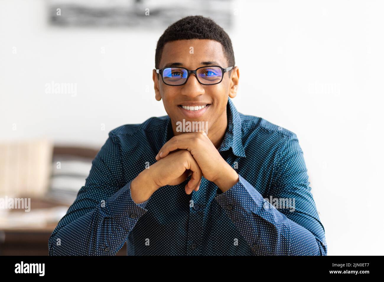 Porträt eines erfolgreichen jungen afroamerikanischen Geschäftsmannes, der im modernen Büro am Arbeitsplatz sitzt Stockfoto