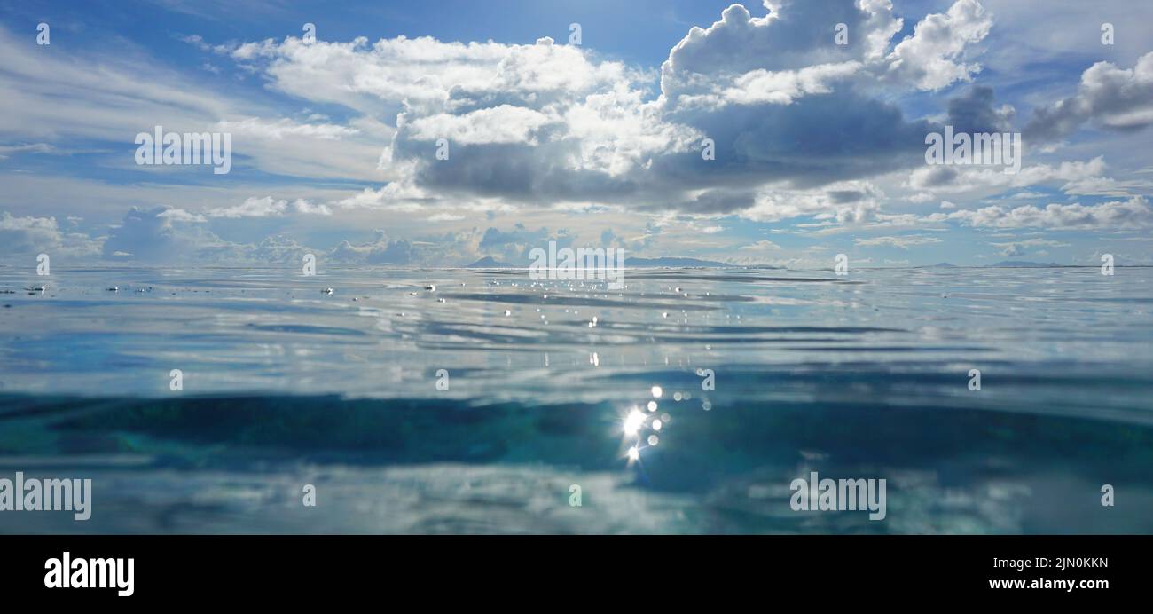 Meeresoberfläche mit Insel am Horizont und blauem Himmel mit Wolken, tropischer Meereslandschaft, Pazifischer Ozean, Französisch-Polynesien Stockfoto