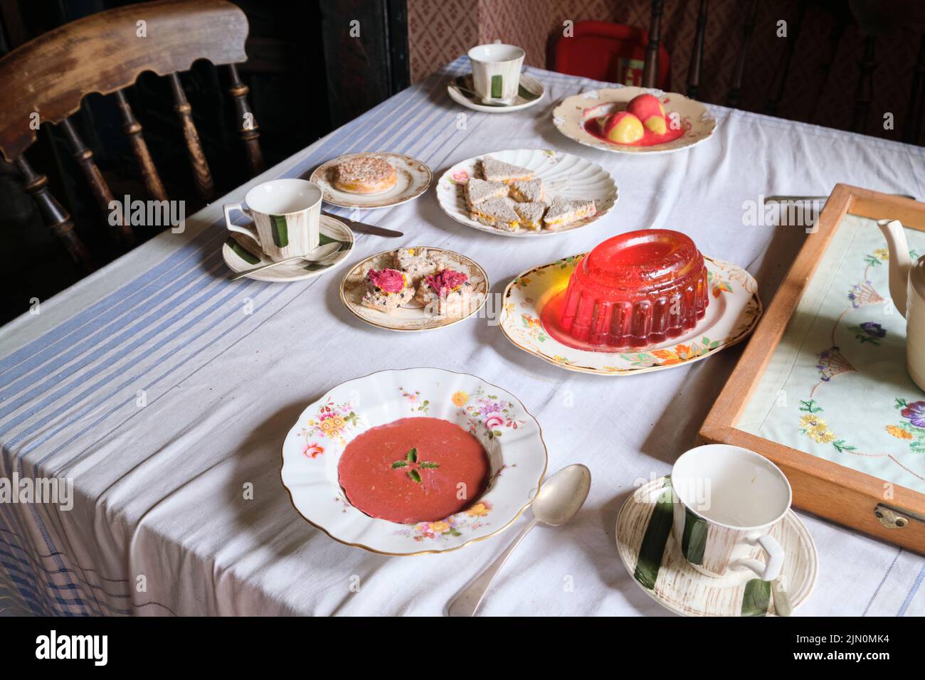 Esstisch mit gefälschten Lebensmitteln aus Kunststoff. Suppe, Jello, Espe, Tee-Sandwiches, Birnen, Scones. In einer Nachbildung eines typischen, generischen Arbeiterhauses, zu Hause Stockfoto