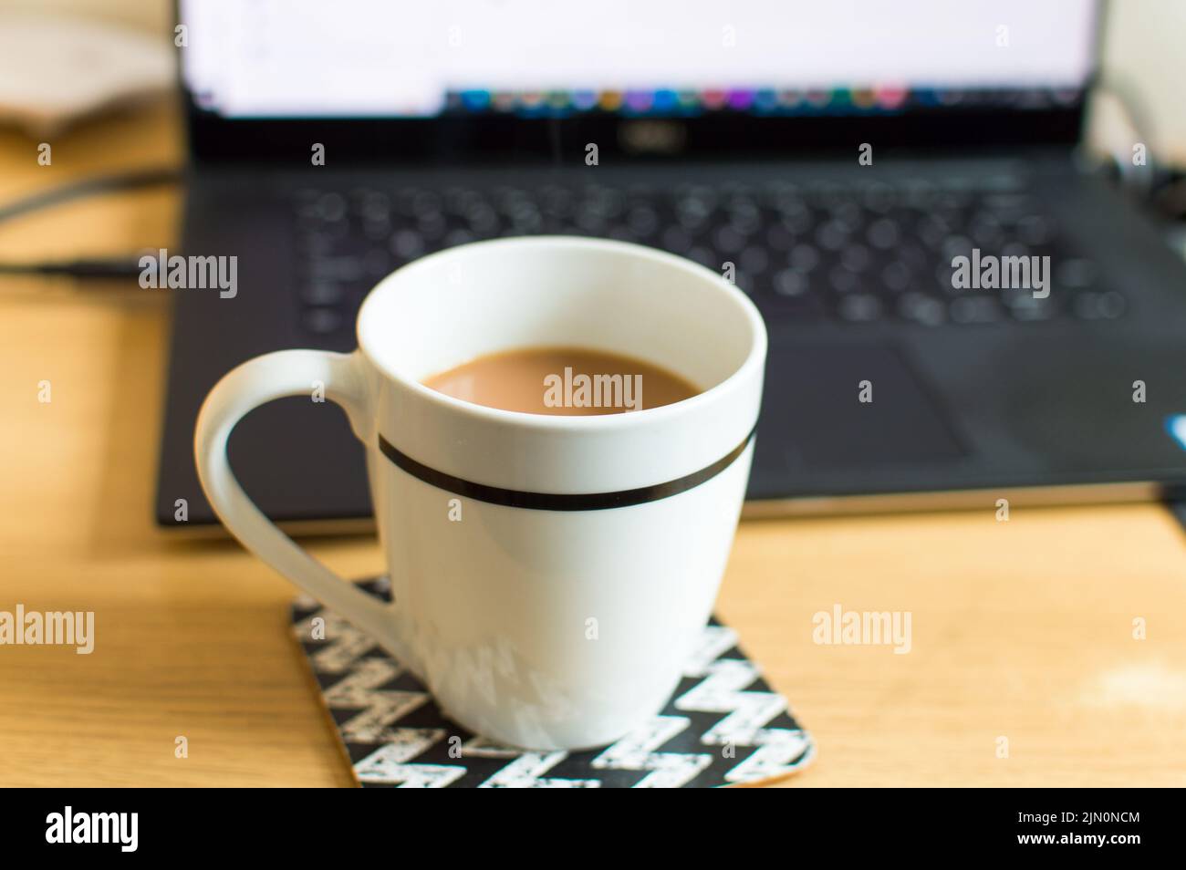 Eine Tasse Tee auf einer Achterbahn neben einem Laptop-Arbeitsplatz Stockfoto