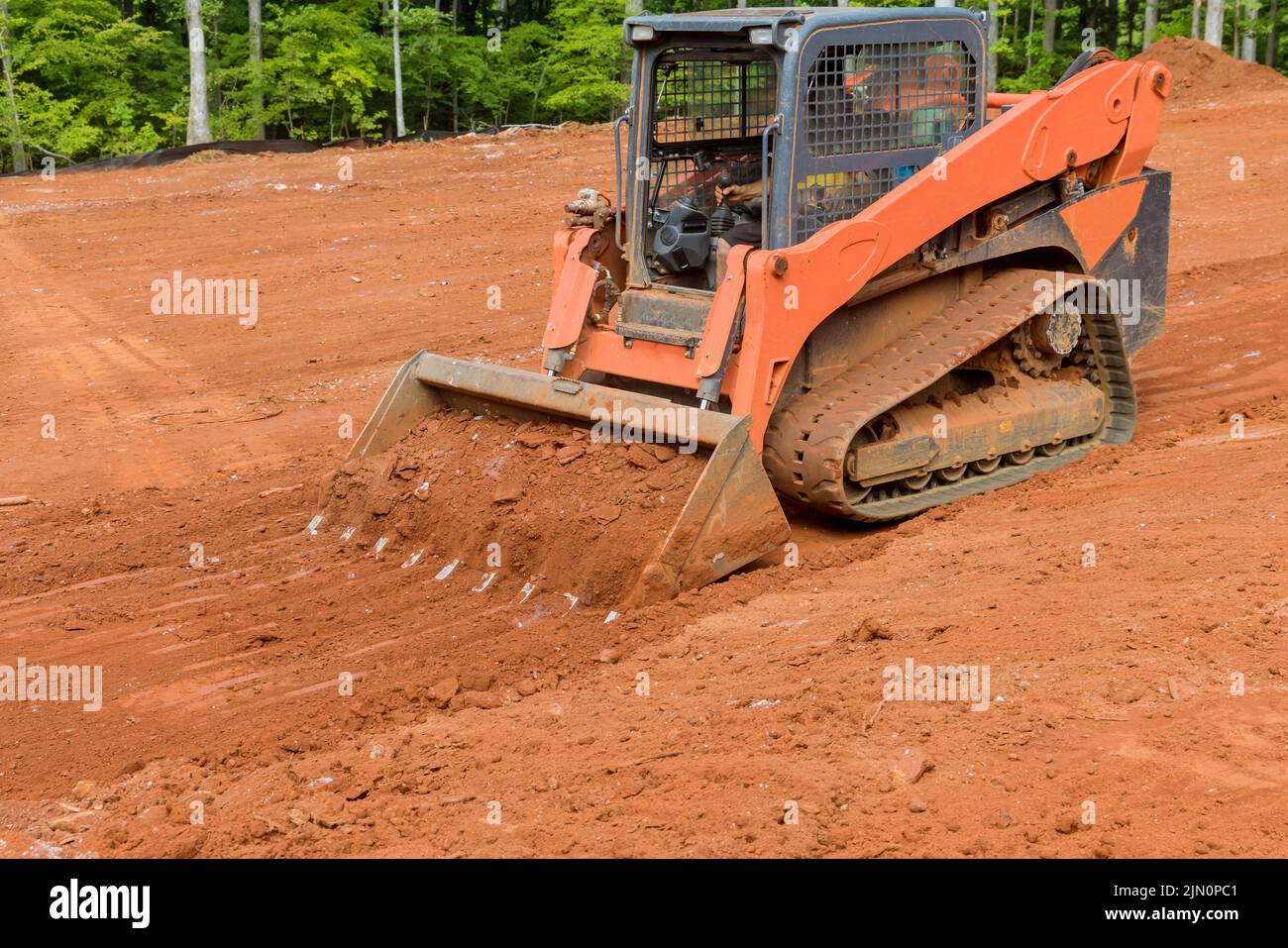 Mithilfe eines kleinen Traktors das Land in der Nähe eines neuen Hauses mit Erdbewegungsgeräten ausgleichen Stockfoto