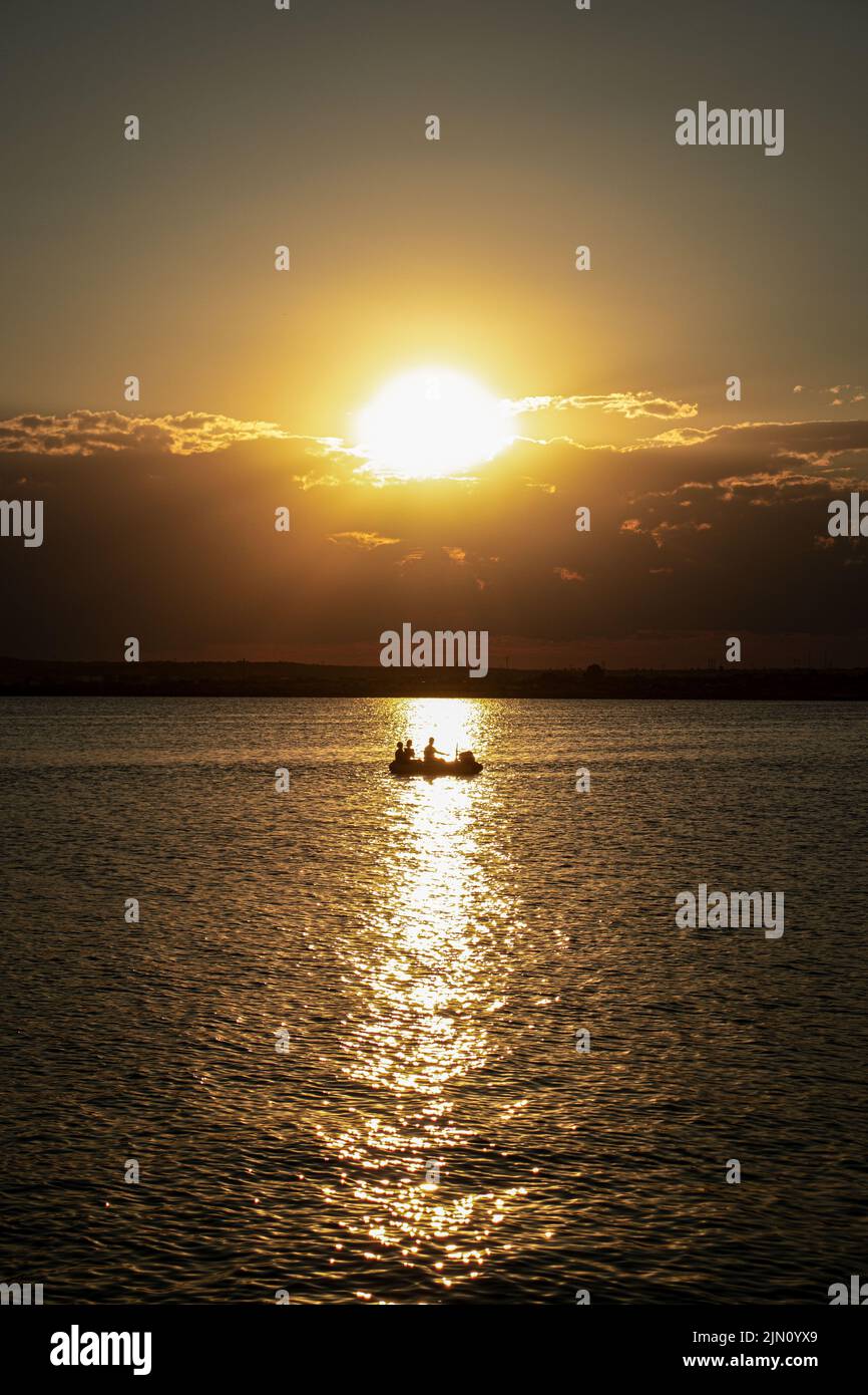 Sonnenuntergang, der sich über die friedlichen Gewässer Griechenlands spiegelt, während ein Boot vorbeifährt Stockfoto