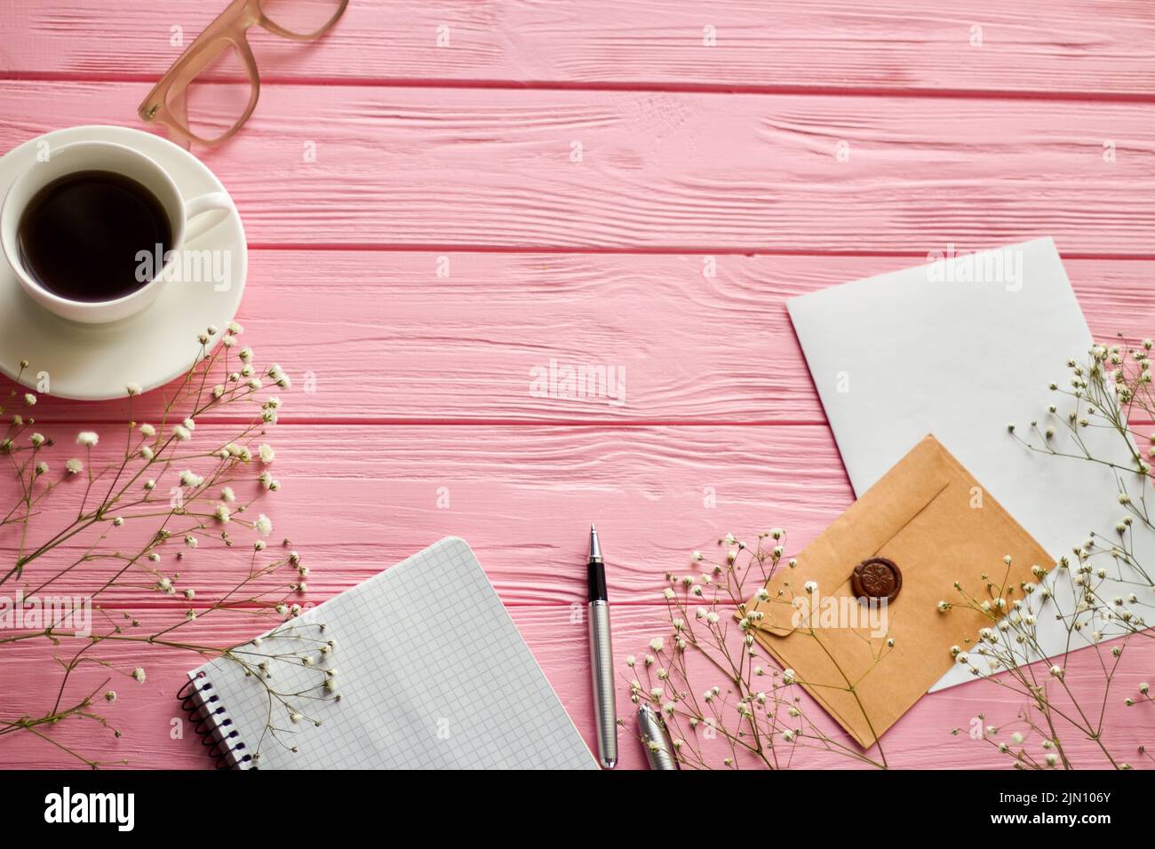 Draufsicht Bürozubehör und Kopierfläche auf rosa Holz. Kaffeetasse mit Notizblock und Umschlag. Stockfoto