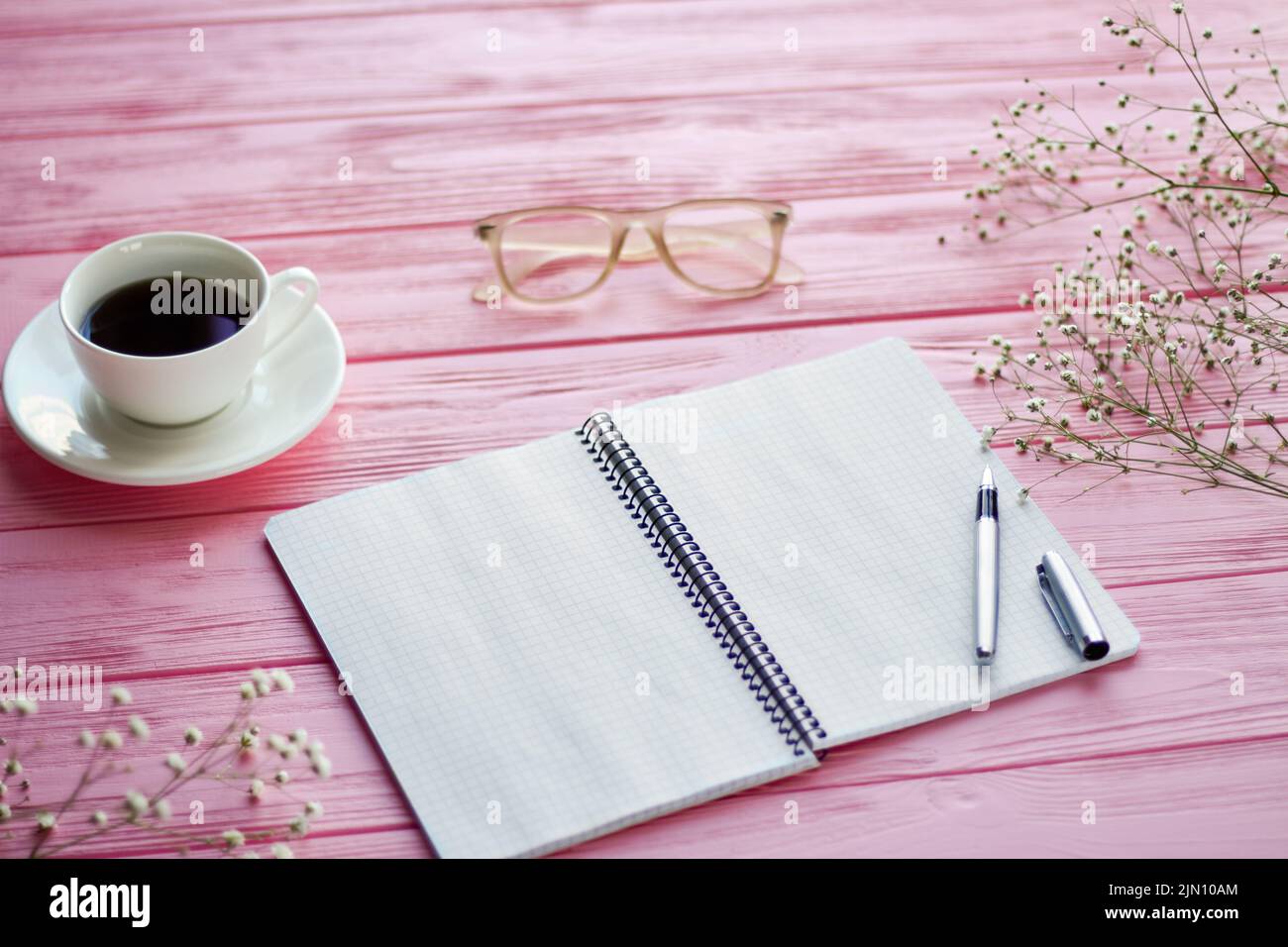 Draufsicht leerer Notizblock mit Kaffeetasse und Gläsern. Schreibtisch aus rosafarbenem Holz. Stockfoto