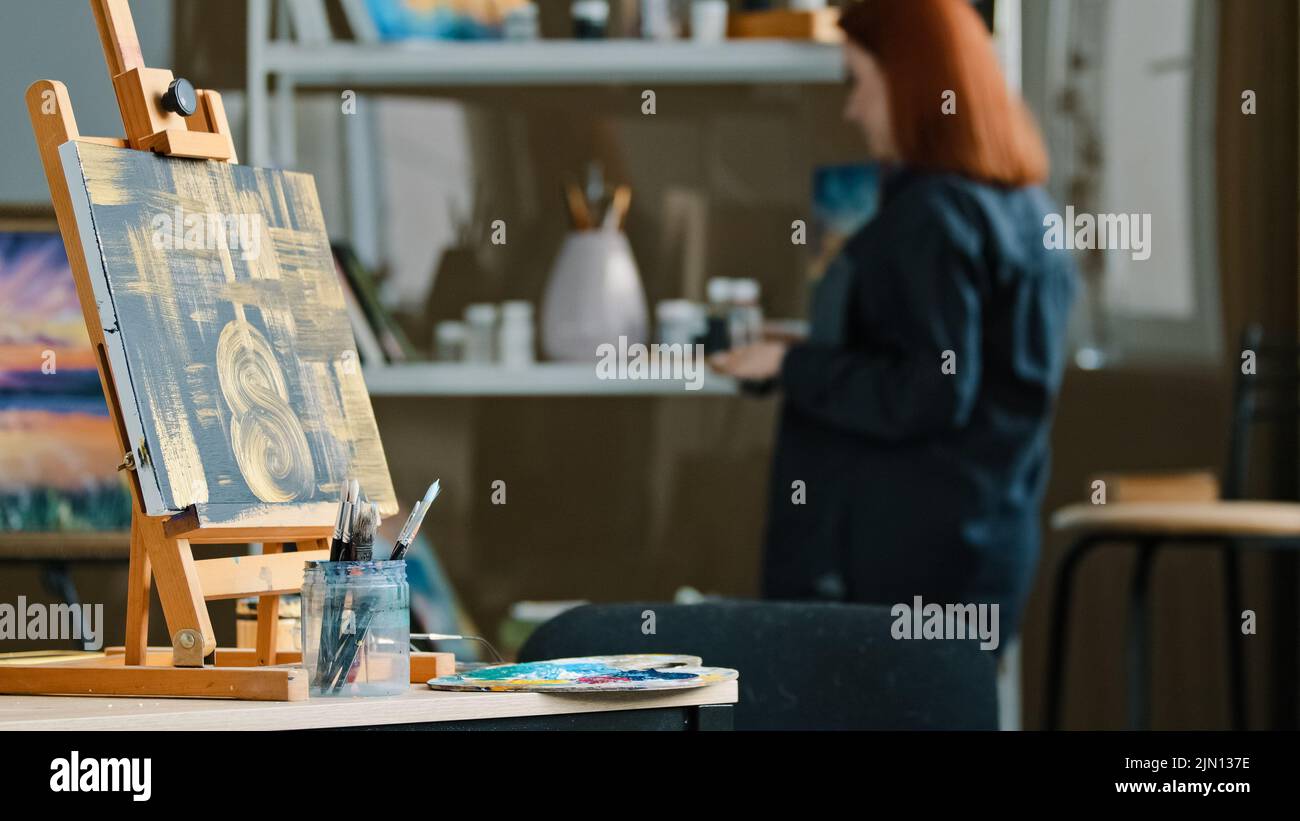 Abstrakte Malerei schwarze Leinwand mit goldenen Zeichnungen auf Staffelei steht auf dem Tisch in Werkstatt-Studio mit Pinsel rothaarige unkenntlich Frau Stockfoto