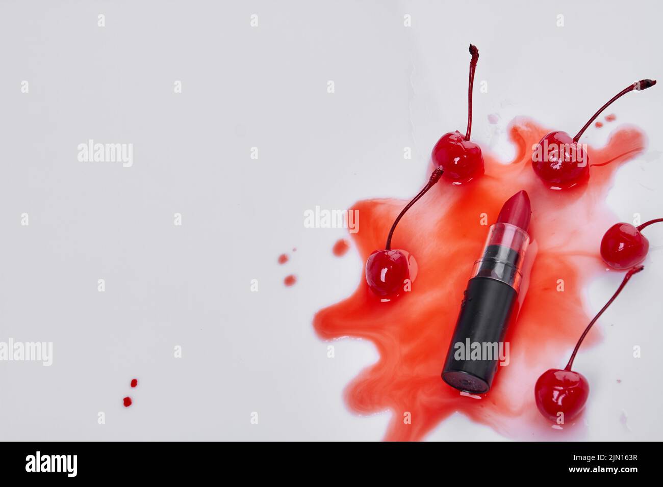 Draufsicht Lippenstift und Kirschen auf roter Flüssigfärbung. Make-up Zubehör auf weißem Hintergrund. Stockfoto