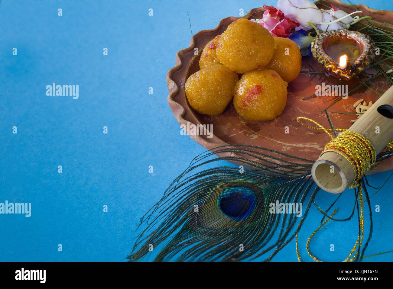 Bambusflöte mit Pfauenfeder verziert, die für den hindu-gott lord krishna mit süßem Laddu, Diya und Blumen während des janmashtami-Fests symbolisch ist Stockfoto