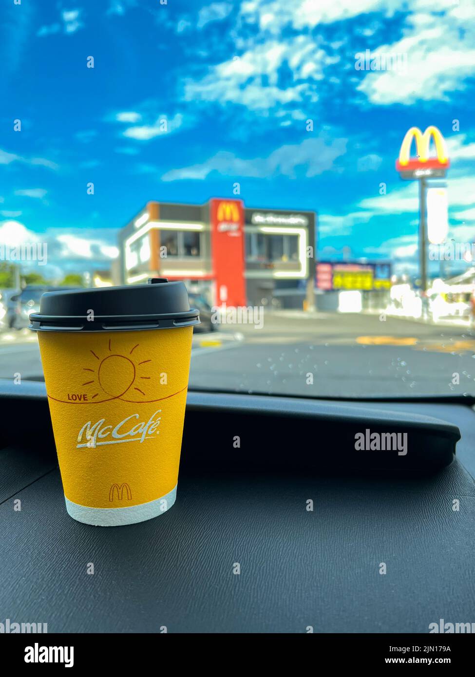 Gelbe Tasse McCafe Japan Kaffee auf dem Armaturenbrett eines Autos, das beim McDonalds Drive-Service gekauft wurde. Stockfoto