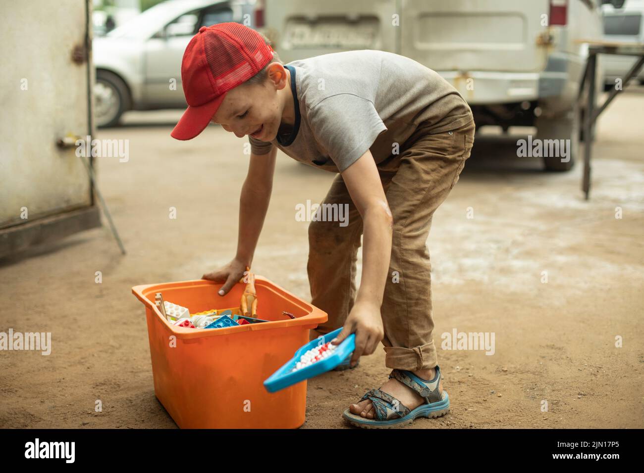 Kind mit Kiste Spielzeug. Junge verstreute Spielsachen. Kind auf der Straße. Stockfoto