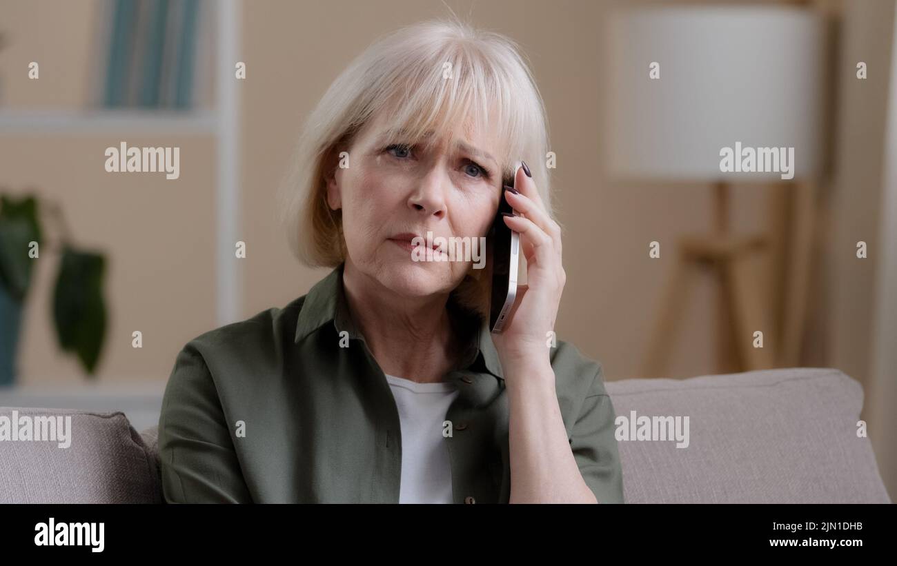 Kaukasische alte Frau reifen mittleren Alters 50s beleidigte Dame im Alter Geschäftsfrau sitzen auf dem Sofa zu Hause hören Stimme auf dem Telefon sprechen Smartphone Stockfoto