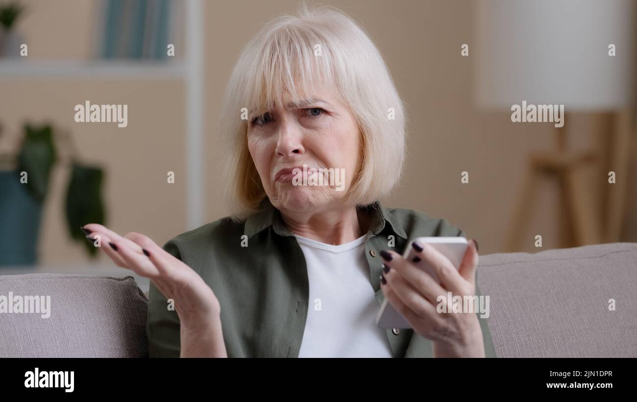 Frustrierte ältere Dame kaukasische ältere Frau mit Telefon liest schlechte Nachrichten in Handy-Nachricht traurig verärgert Schock Scheitern mit Smartphone-App. Besorgt Stockfoto