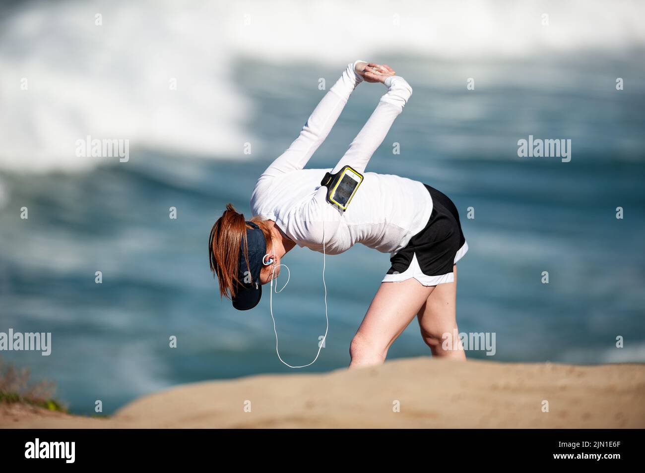 Das Bild einer Frau, die sich vor ihrem morgendlichen Strandlauf streckt. Nächstplatzierter Wärmt Sich Auf, Beach Runner, San Francisco, Kalifornien, Gesundheit, Wellness, Sport Stockfoto