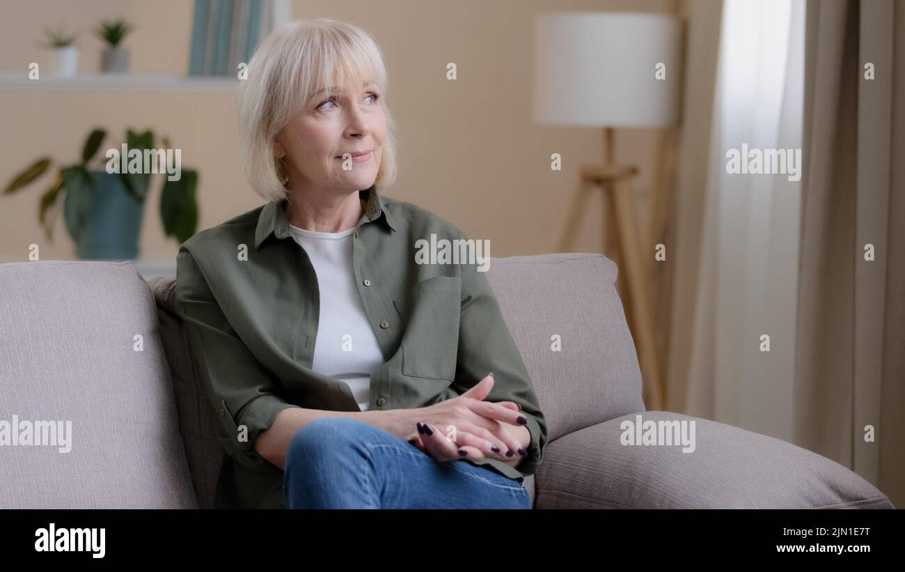 Glücklich träumen inspiriert nachdenkliche ältere alte kaukasische 60s Frau schaut weg im Fenster sitzen auf dem Sofa allein denken, nachdenkliche ältere Dame mittleren Alters Stockfoto
