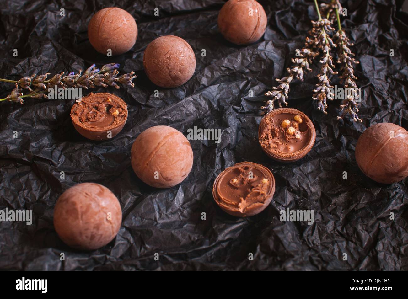 Schokoladen-Bonbons auf dunklem zerknittertem Bastelpapier mit Lavendelblüten Stockfoto