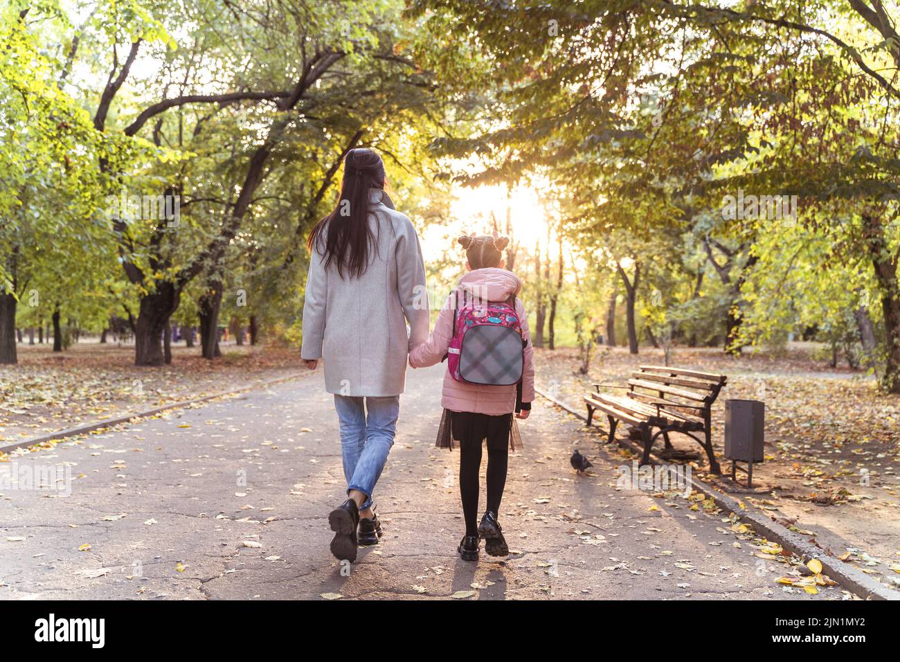 Mutter und Tochter gehen im Herbstpark spazieren. Kleines Mädchen nach der Schule mit Mutter von hinten. Alltag Stockfoto