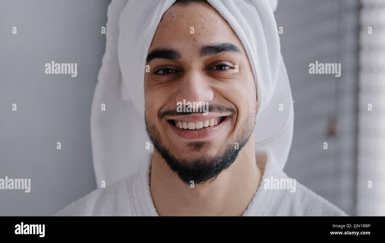 Nahaufnahme männliches Gesicht mit Akne Kopfschuss Porträt lächelnd toothy schöner arabisch indischer bärtiger Mann mit Badetuch auf dem Kopf stehend im Badezimmer. Gesund Stockfoto